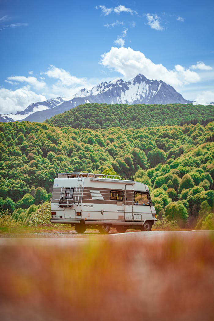 A classic camper van parked in front of a majestic snow-capped mountain range under a bright blue sky.
